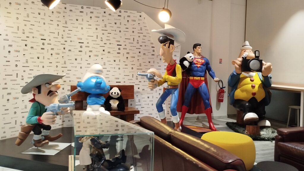 Photographie de l'accueil de Media Participation où se trouve le bureau de Sarah Neme. Nous y retrouvons des statues grandeur nature des héros qui ont marqué des générations comme Lucky Luck et Superman.